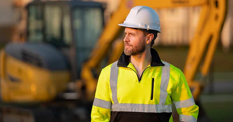Construction worker wearing a yellow vest standing in front of excavators